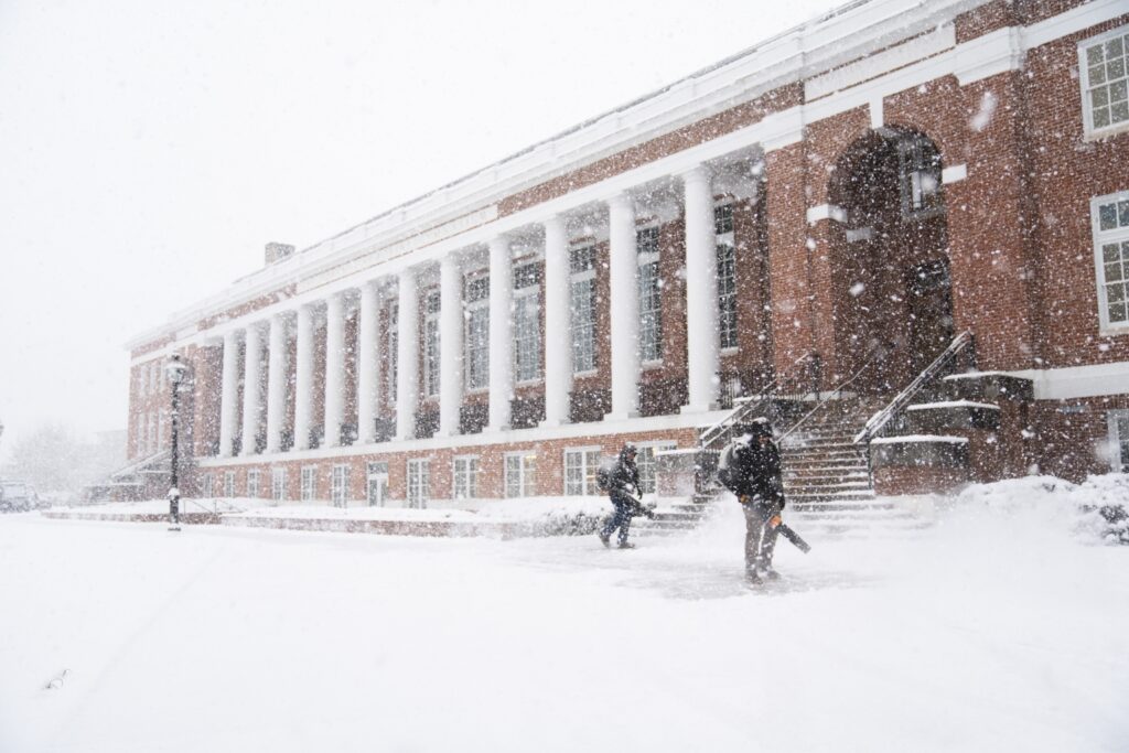 Snow falling on Cannan Green with workers clearing the sidewalks with blowers.